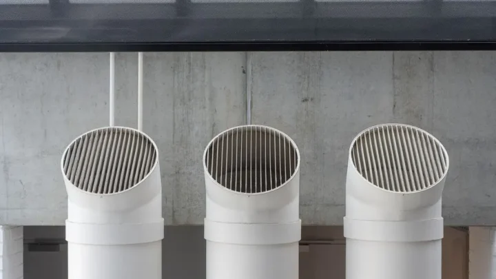 Three white ventilation pipes along a concrete wall